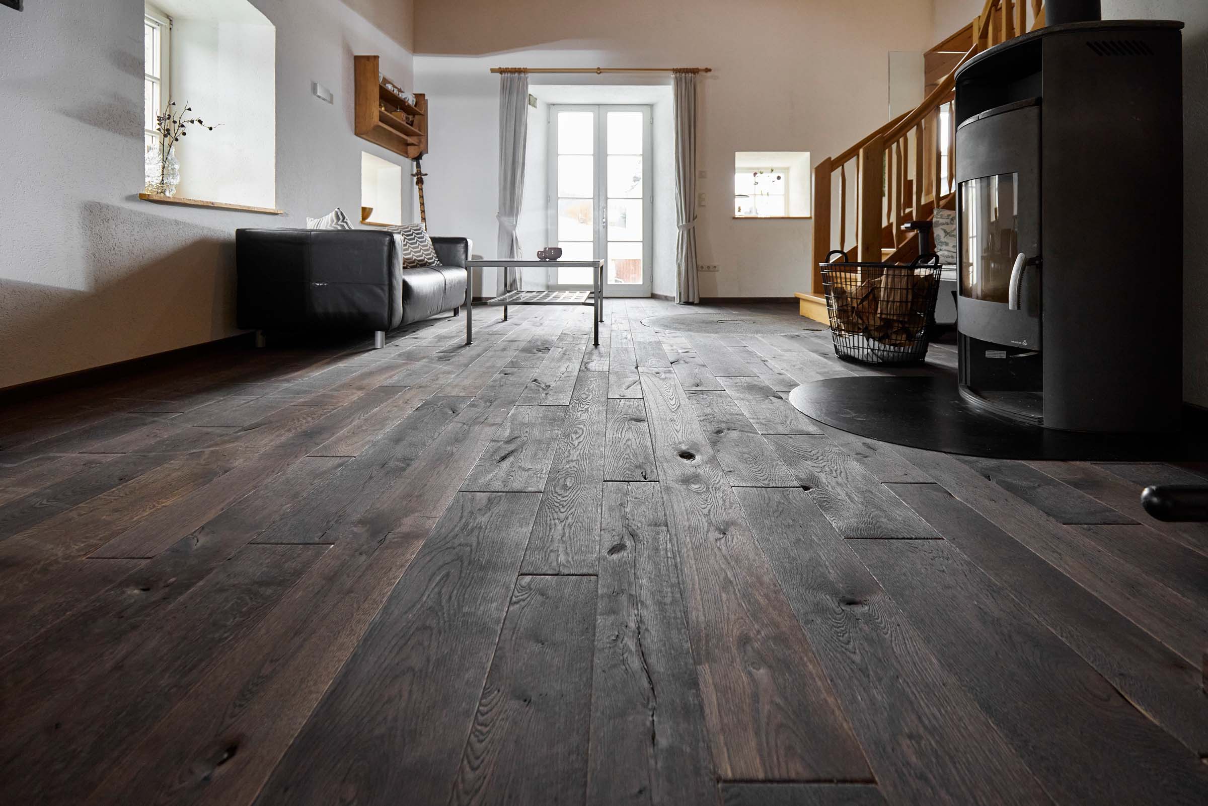 Wohnzimmer mit rustikalem Mühlenboden in dunkler Ausführung, moderner Einrichtung und Kaminofen in der renovierten alten Mühle.