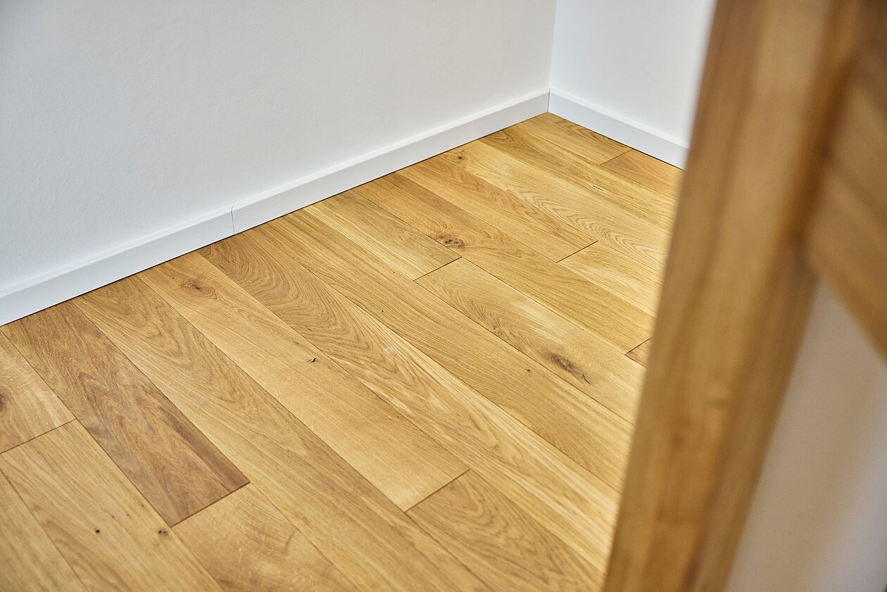Weiß lackierte Sockelleiste im Profil 1 oder 2 an einer hellen Wand, kombiniert mit einer Massivholzdiele aus Eiche.