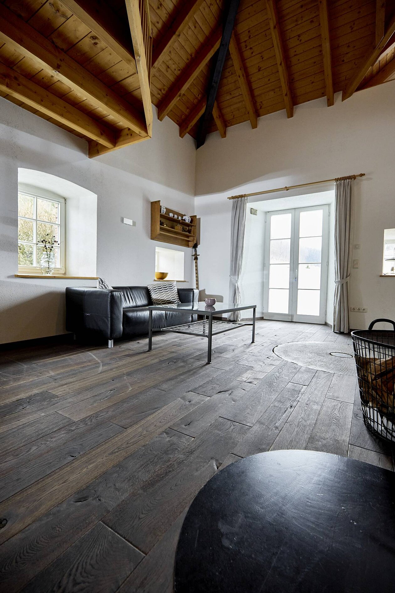 Wohnraum mit historischem Mühlenboden aus dunkler Eiche, rustikaler Einrichtung und Blick auf die erhaltene Rundung des alten Mühlsteins im Boden.